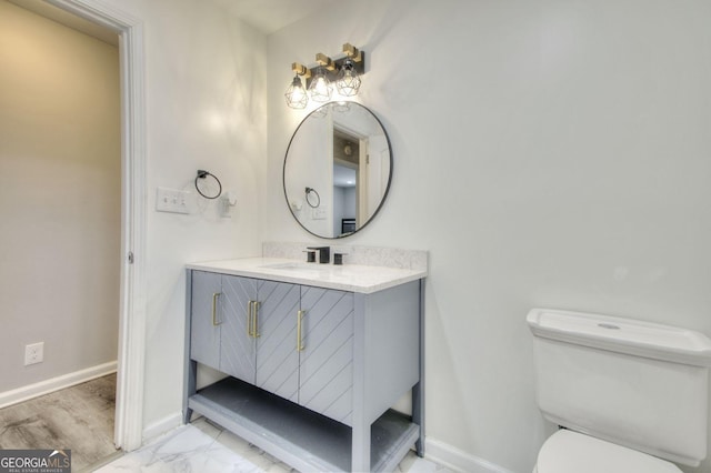 half bathroom featuring toilet, marble finish floor, baseboards, and vanity