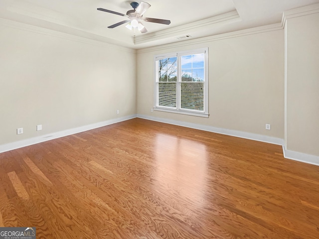 empty room with a tray ceiling, visible vents, a ceiling fan, wood finished floors, and baseboards