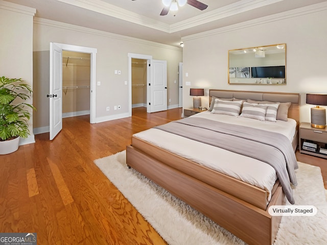 bedroom featuring baseboards, a ceiling fan, wood finished floors, a walk in closet, and crown molding