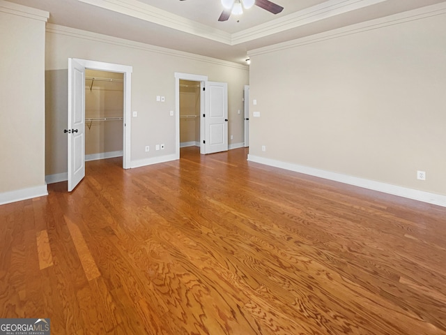 unfurnished bedroom featuring baseboards, ornamental molding, light wood-type flooring, a walk in closet, and a raised ceiling