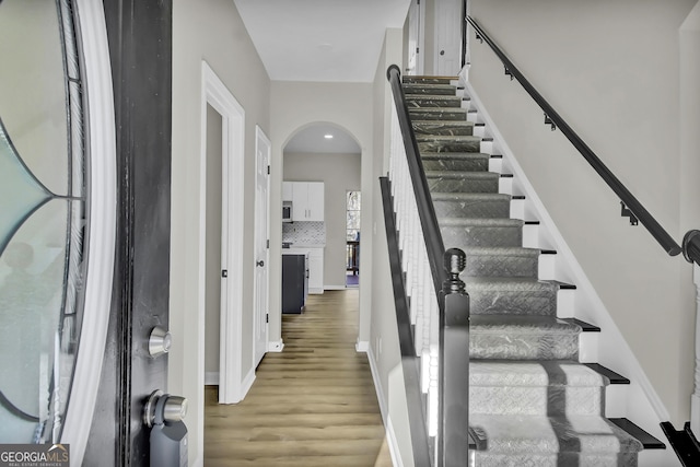 entryway with arched walkways, baseboards, and light wood-style floors