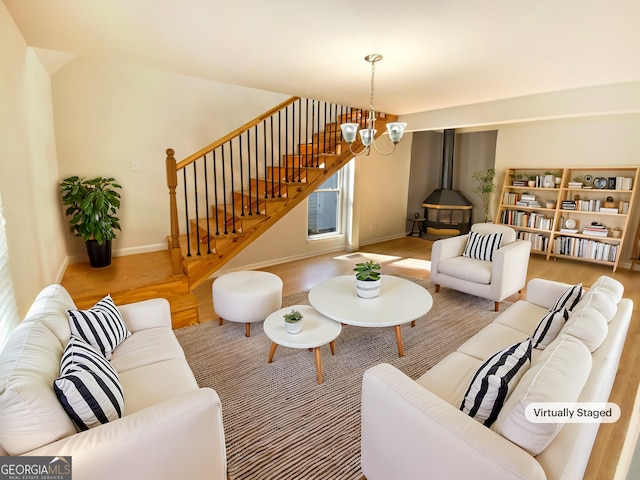 living area with stairway, an inviting chandelier, a wood stove, wood finished floors, and baseboards