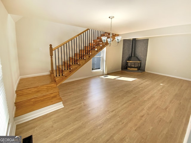 unfurnished living room featuring baseboards, stairway, wood finished floors, a wood stove, and a notable chandelier