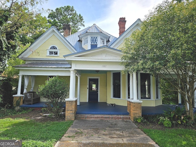 view of front of house with a porch, metal roof, and a chimney