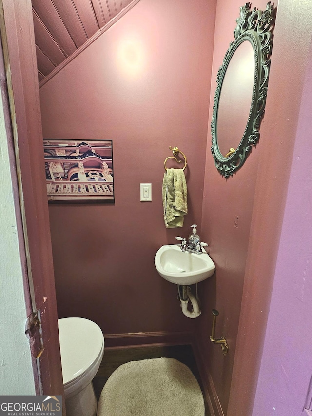 half bath with toilet, baseboards, vaulted ceiling, and a sink