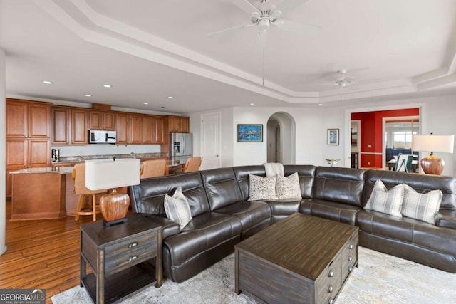 living room featuring wood finished floors, recessed lighting, arched walkways, ceiling fan, and a raised ceiling