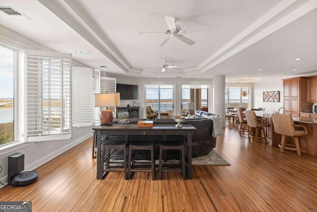 living area featuring wood finished floors, visible vents, baseboards, a tray ceiling, and recessed lighting