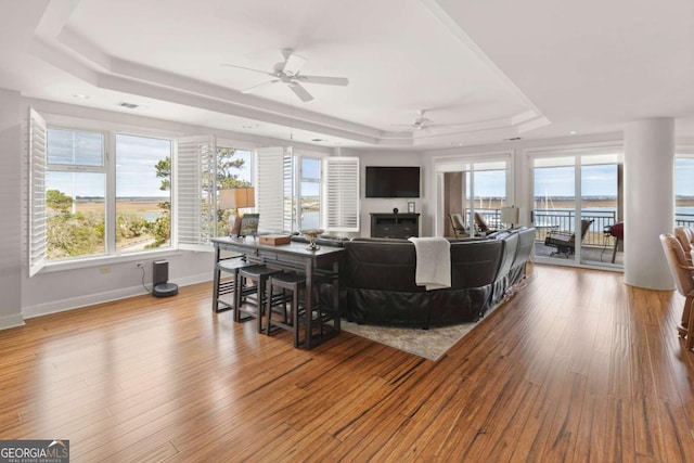 living area with baseboards, a tray ceiling, a fireplace, ceiling fan, and hardwood / wood-style flooring