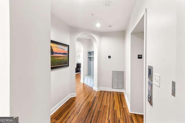 hall with arched walkways, visible vents, baseboards, and wood-type flooring