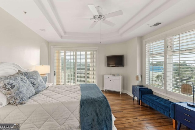 bedroom with wood finished floors, visible vents, baseboards, a tray ceiling, and access to exterior