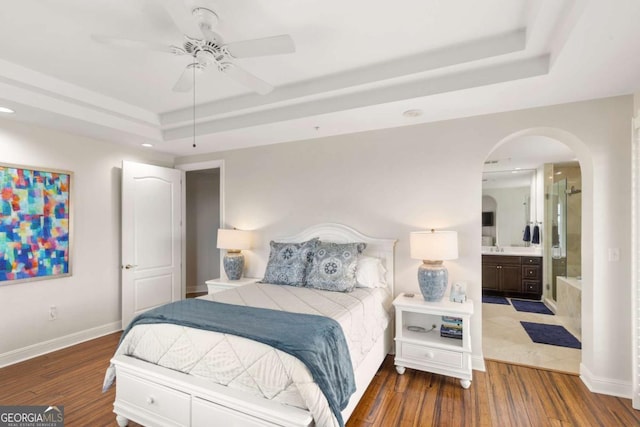 bedroom with baseboards, a raised ceiling, arched walkways, and wood finished floors