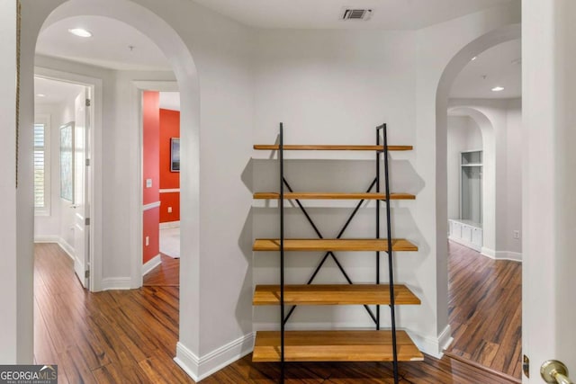 hallway with visible vents, wood finished floors, recessed lighting, arched walkways, and baseboards