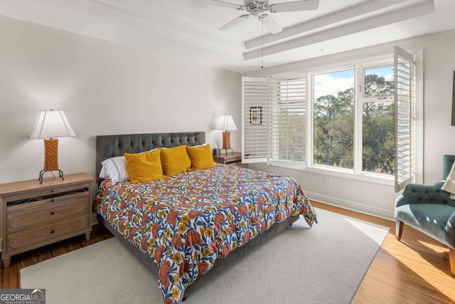 bedroom with multiple windows, a raised ceiling, baseboards, and wood finished floors