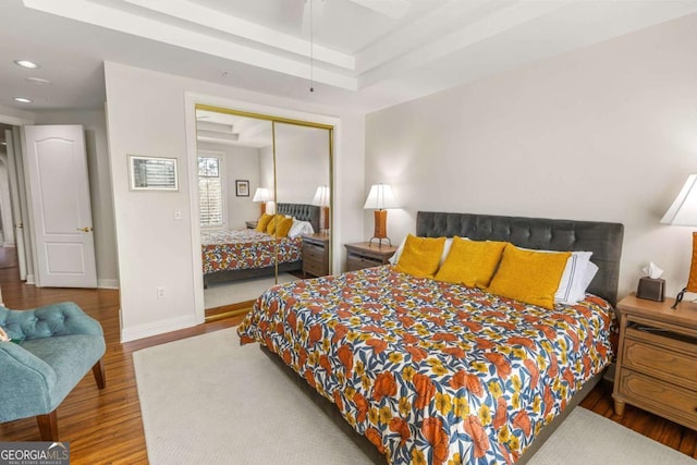 bedroom with a tray ceiling, wood finished floors, a closet, and baseboards