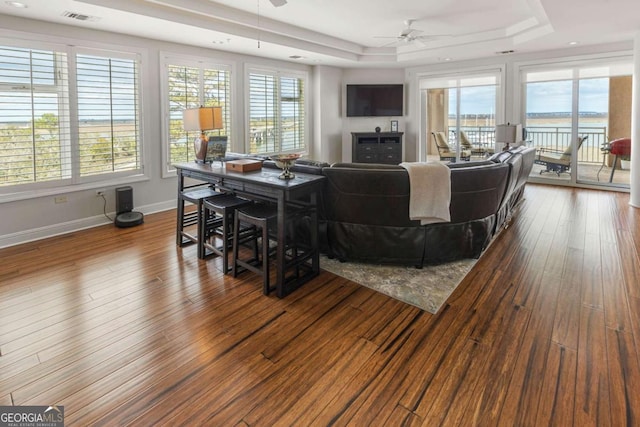 living room with a wealth of natural light, a tray ceiling, and dark wood-style floors