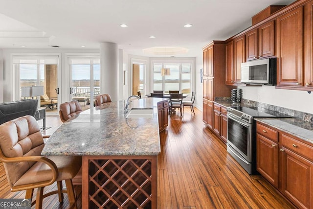 kitchen featuring a sink, open floor plan, a breakfast bar area, stainless steel appliances, and dark wood-style flooring