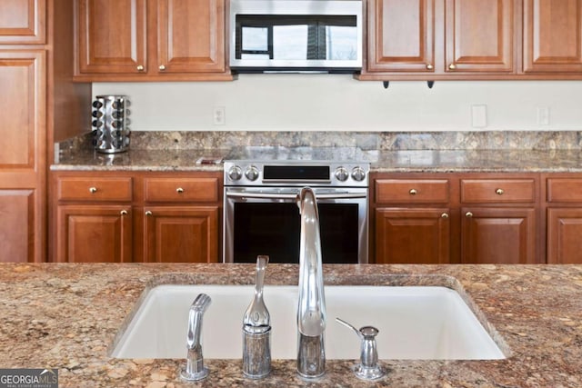 kitchen featuring a sink, brown cabinetry, light stone countertops, and stainless steel appliances