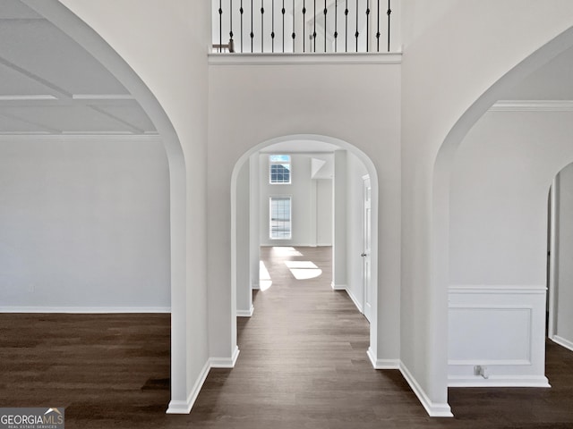 hall featuring a towering ceiling, baseboards, and dark wood finished floors