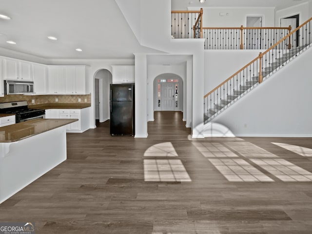 kitchen featuring arched walkways, dark wood-style floors, appliances with stainless steel finishes, open floor plan, and white cabinetry