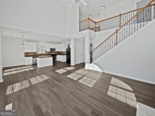 unfurnished living room with dark wood-style flooring, stairway, baseboards, and ceiling fan with notable chandelier