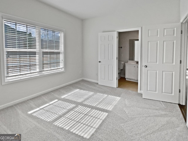 unfurnished bedroom with baseboards, light tile patterned floors, ensuite bathroom, and light colored carpet