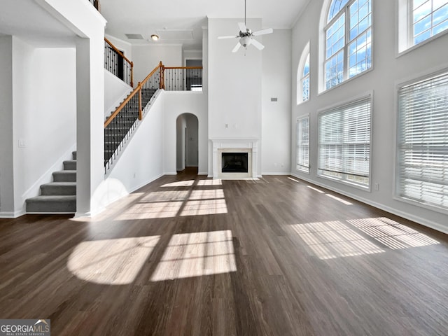 unfurnished living room featuring ceiling fan, a fireplace, wood finished floors, baseboards, and stairs