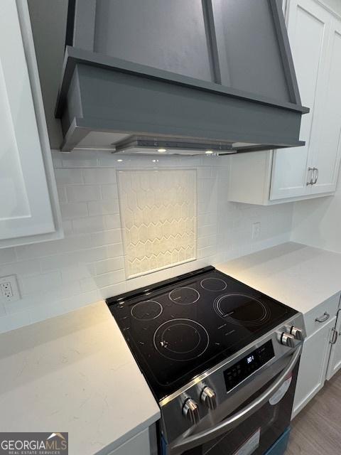kitchen featuring decorative backsplash, white cabinetry, electric range, and wall chimney exhaust hood