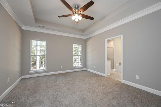 carpeted spare room featuring a tray ceiling, a ceiling fan, visible vents, and baseboards