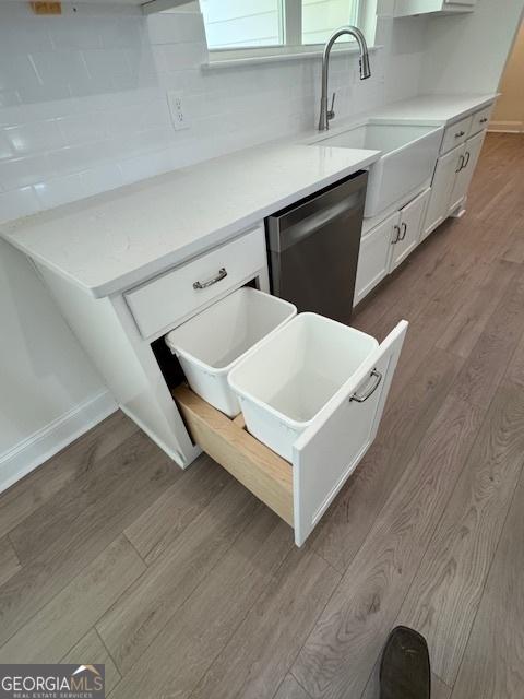interior details featuring a sink, stainless steel dishwasher, wood finished floors, and baseboards