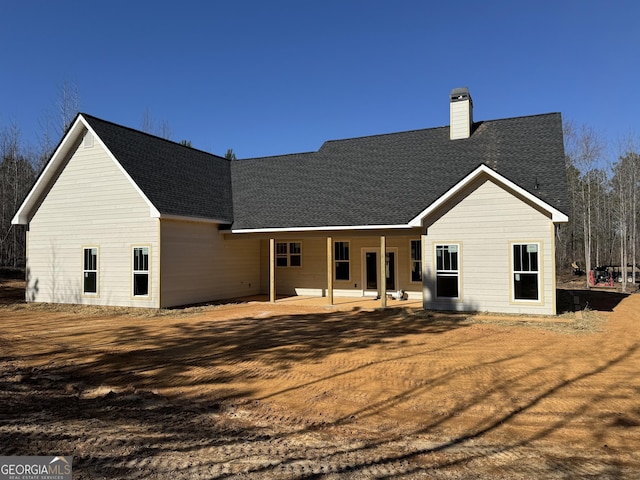 back of house featuring a patio, roof with shingles, and a chimney