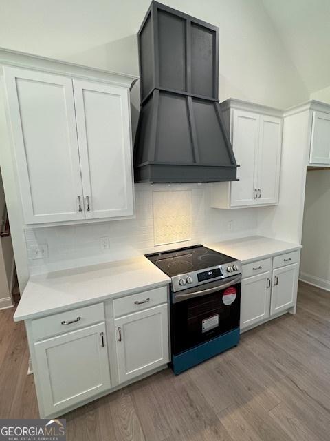kitchen with custom exhaust hood, white cabinets, light countertops, light wood-type flooring, and electric range