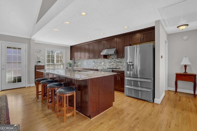 kitchen featuring a kitchen island with sink, under cabinet range hood, a sink, stainless steel fridge with ice dispenser, and tasteful backsplash