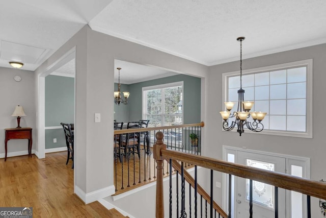 hall with ornamental molding, a notable chandelier, and light wood-style flooring