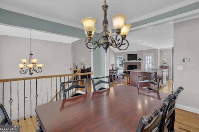 dining space featuring a notable chandelier, light wood finished floors, ornamental molding, a brick fireplace, and baseboards