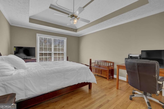 bedroom featuring a tray ceiling, light wood finished floors, ornamental molding, a textured ceiling, and baseboards