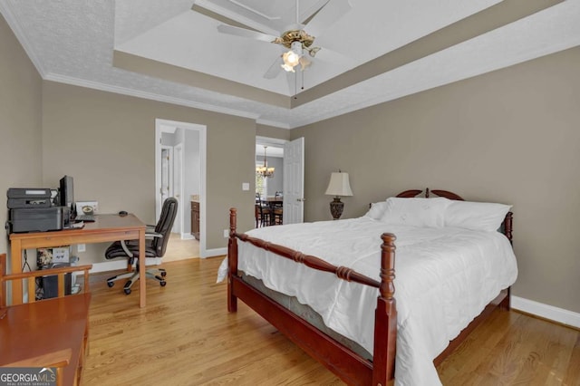 bedroom with baseboards, a raised ceiling, ornamental molding, an inviting chandelier, and light wood-type flooring