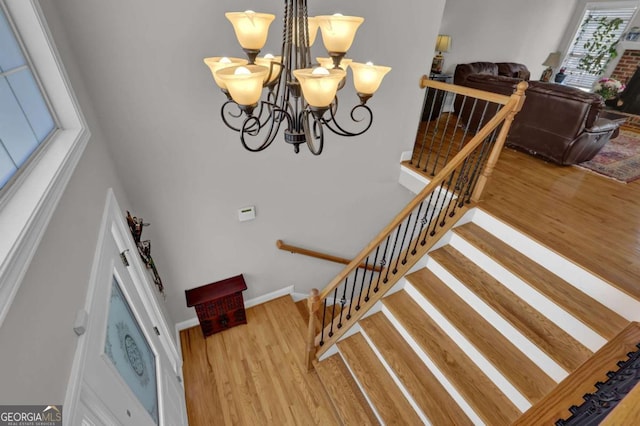 staircase with an inviting chandelier, baseboards, and wood finished floors