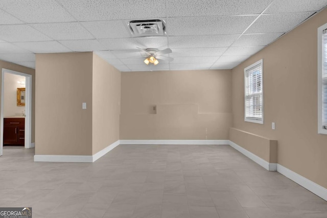 empty room featuring a ceiling fan, visible vents, a drop ceiling, and baseboards