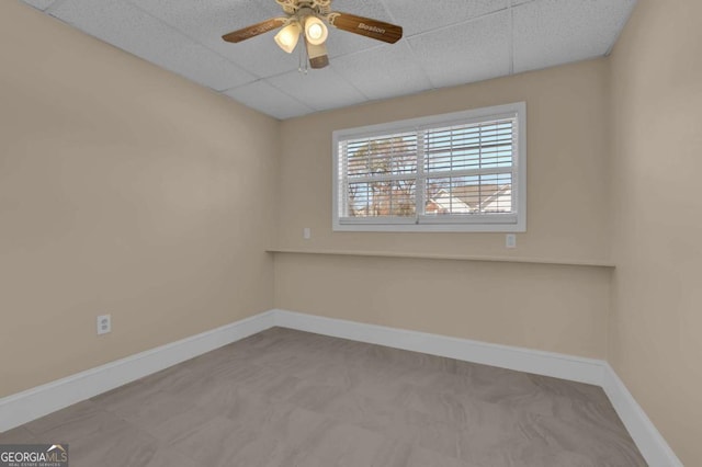 empty room with a drop ceiling, a ceiling fan, and baseboards