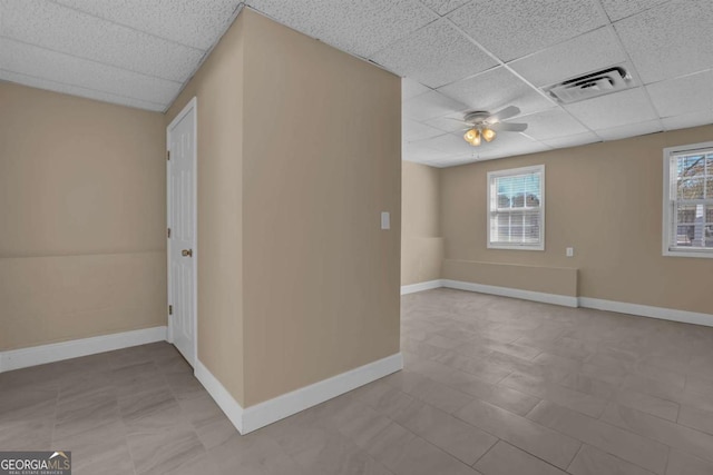 empty room with a ceiling fan, a drop ceiling, visible vents, and baseboards