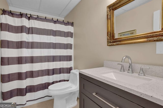 full bath with toilet, a shower with curtain, a paneled ceiling, and vanity