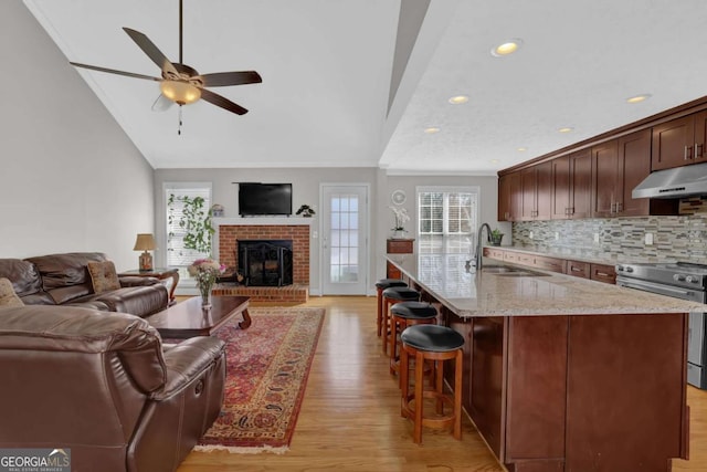 kitchen featuring electric range, open floor plan, an island with sink, light stone countertops, and under cabinet range hood