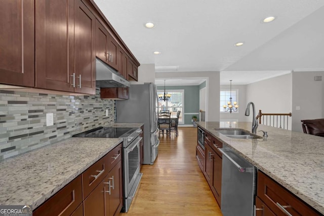 kitchen with pendant lighting, stainless steel appliances, a sink, light stone countertops, and under cabinet range hood