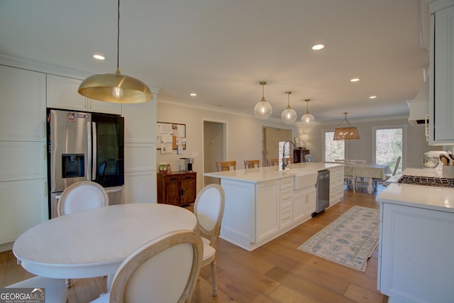 kitchen featuring stainless steel appliances, a sink, white cabinets, ornamental molding, and light wood finished floors