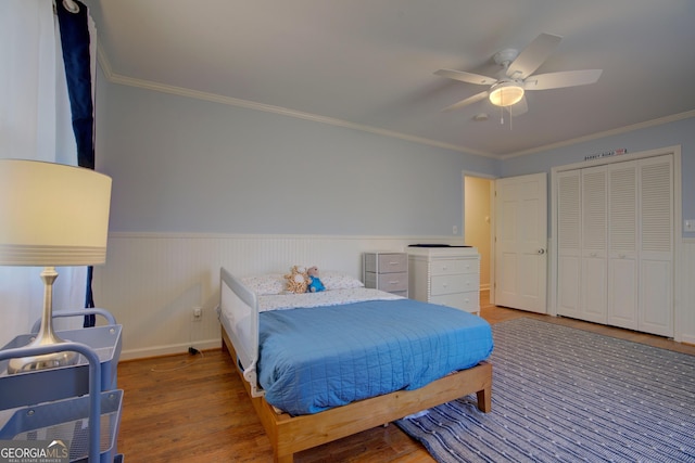 bedroom featuring a wainscoted wall, ornamental molding, wood finished floors, and a ceiling fan