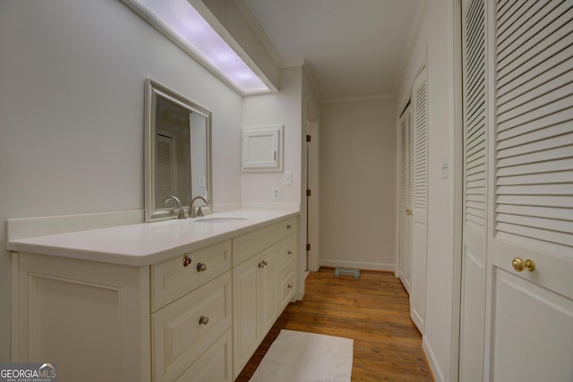 bathroom with baseboards, wood finished floors, crown molding, vanity, and a closet