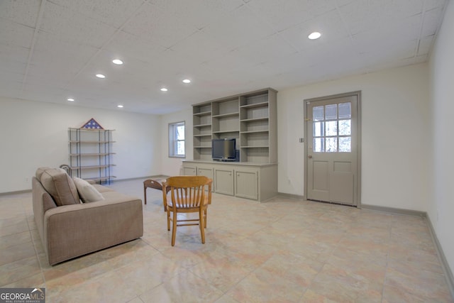 living room featuring baseboards, a drop ceiling, and recessed lighting