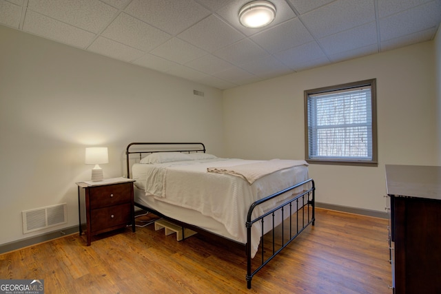 bedroom featuring baseboards, visible vents, a drop ceiling, and wood finished floors