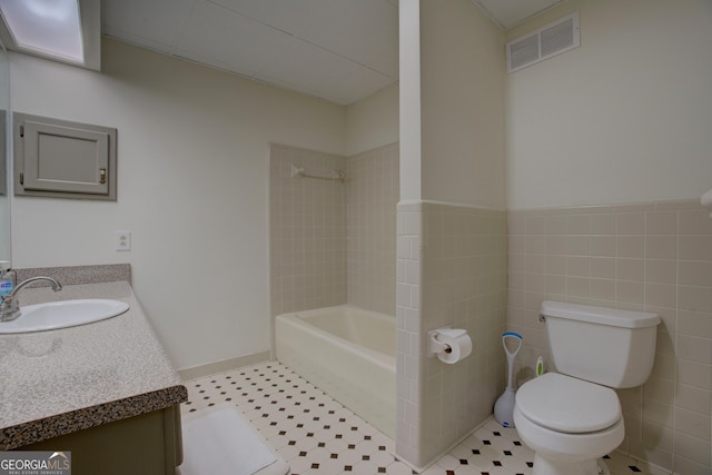 full bath with visible vents, bathing tub / shower combination, toilet, vanity, and tile walls