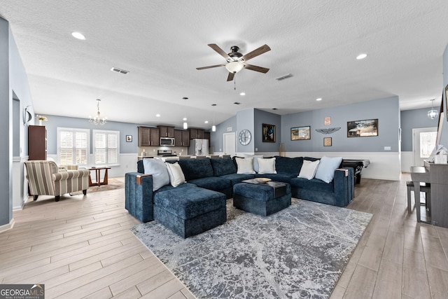 living room with a textured ceiling, light wood finished floors, ceiling fan with notable chandelier, and visible vents